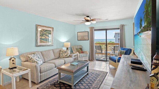 A living room with a sofa, coffee table, and TV, a balcony with a view, and a ceiling fan. - Spacious condo, across the street from the beach + Free Attraction Tickets! (North Myrtle Beach)