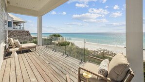 Ein Holzdeck mit Glastrennwand mit Blick auf einen Strand.