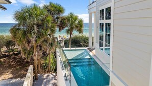 Ein Pool neben einem Gebäude mit großen Fenstern, mit Blick auf einen Strand und den Ozean.