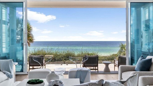 Ein modernes Wohnzimmer mit einem großen Glasfenster, das auf einen Balkon mit Blick auf einen Strand führt.