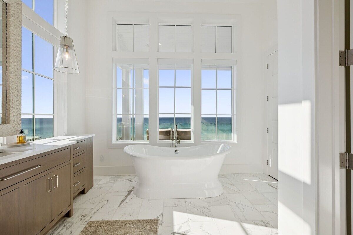 A modern bathroom with a freestanding bathtub, large windows, and a marble floor.