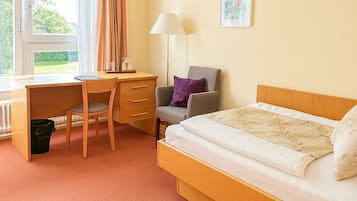 Ein Schlafzimmer mit Bett, Schreibtisch, Stuhl, Lampe und Heizkörper.