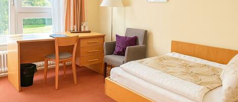 A bedroom with a bed, a desk, a chair, a lamp, and a radiator.
