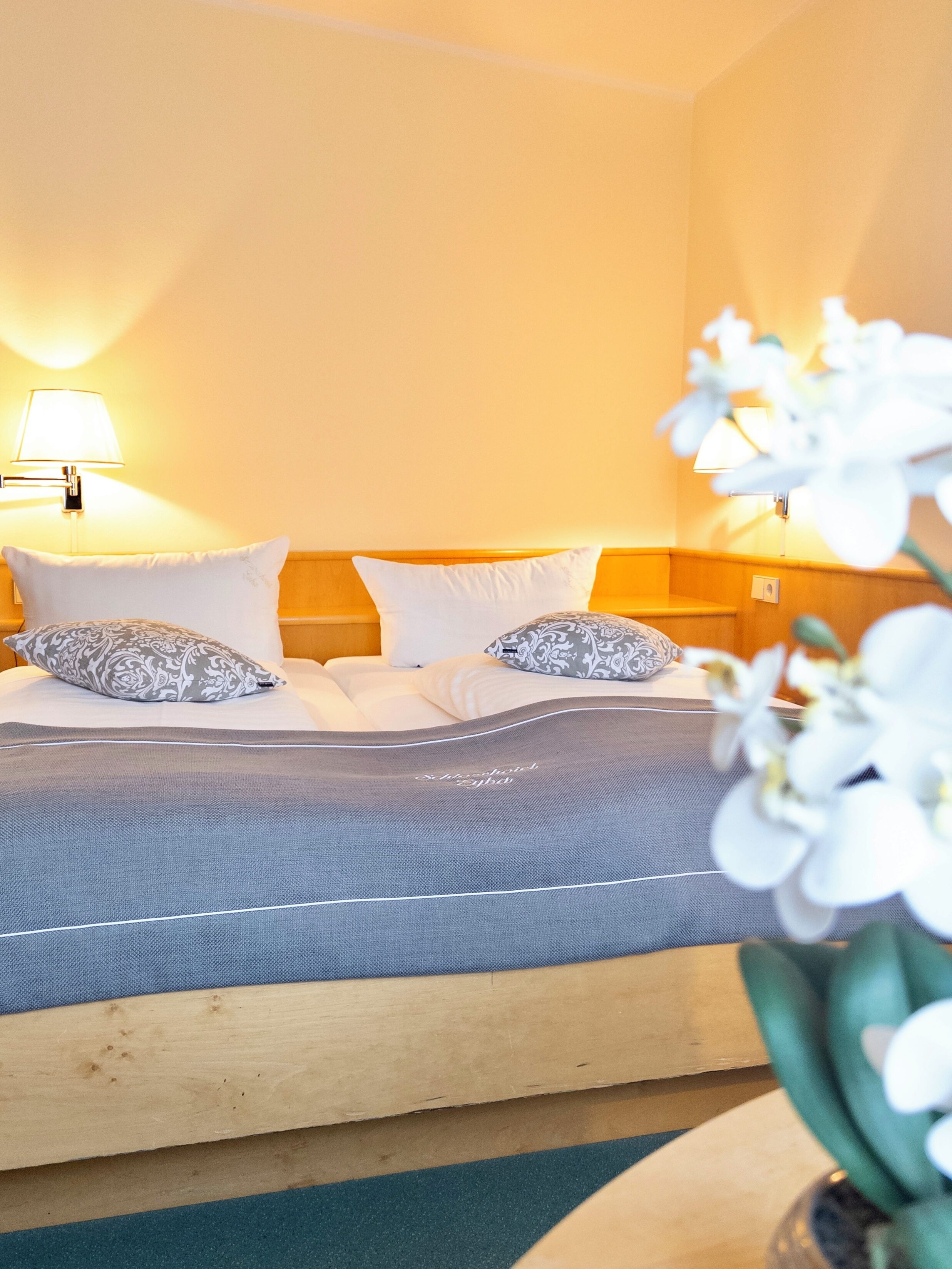 A hotel room with a bed, two bedside lamps, and a floral arrangement.