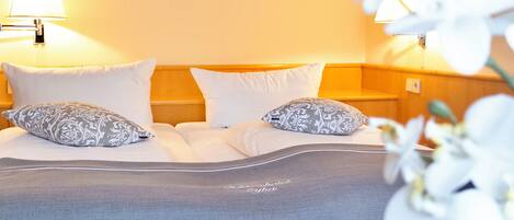 A hotel room with a bed, two bedside lamps, and a floral arrangement.