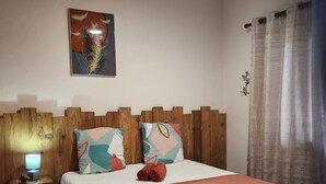 Habitación de hotel con cabecera de madera, cama con manta roja, mesita de noche con lámpara y una obra de arte colgada en la pared.