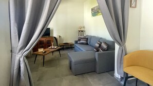 Una sala de estar con cortinas grises, un sofá, una mesa de centro y un sillón amarillo.