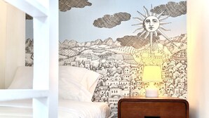 A bedroom with a bed, a nightstand, and a wall mural depicting a cityscape with a sun.