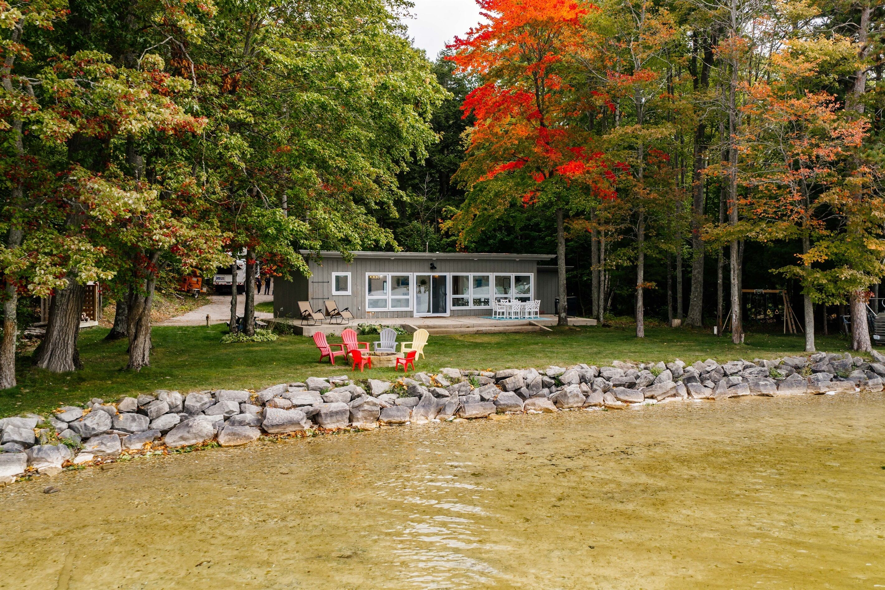 Une cabane avec un mur en pierre et une pelouse, entourée d’arbres aux feuilles d’automne.