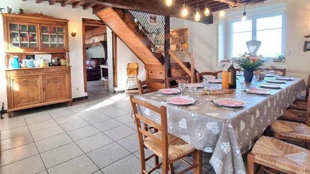 Un coin repas avec une table en bois dressée pour quatre personnes, un escalier et un espace cuisine avec des placards.