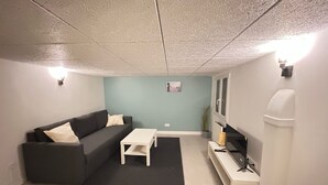 Una sala de estar moderna con un sofá gris, una mesa de centro blanca y un televisor sobre un mueble blanco.