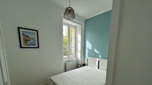 Un dormitorio con una cama, una ventana, un cuadro en la pared y una lámpara colgante.