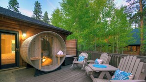 Een houten terras met een sauna, zitplaatsen buiten en uitzicht op het omliggende bos.
