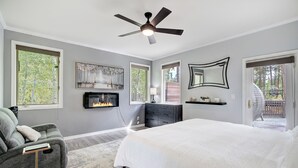 Een slaapkamer met een bed, een grijze bank, een open haard, een plafondventilator en grote ramen.