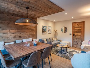 Una sala de estar moderna con techo de madera, una mesa de comedor con sillas, un sofá y una mesa redonda de centro.
