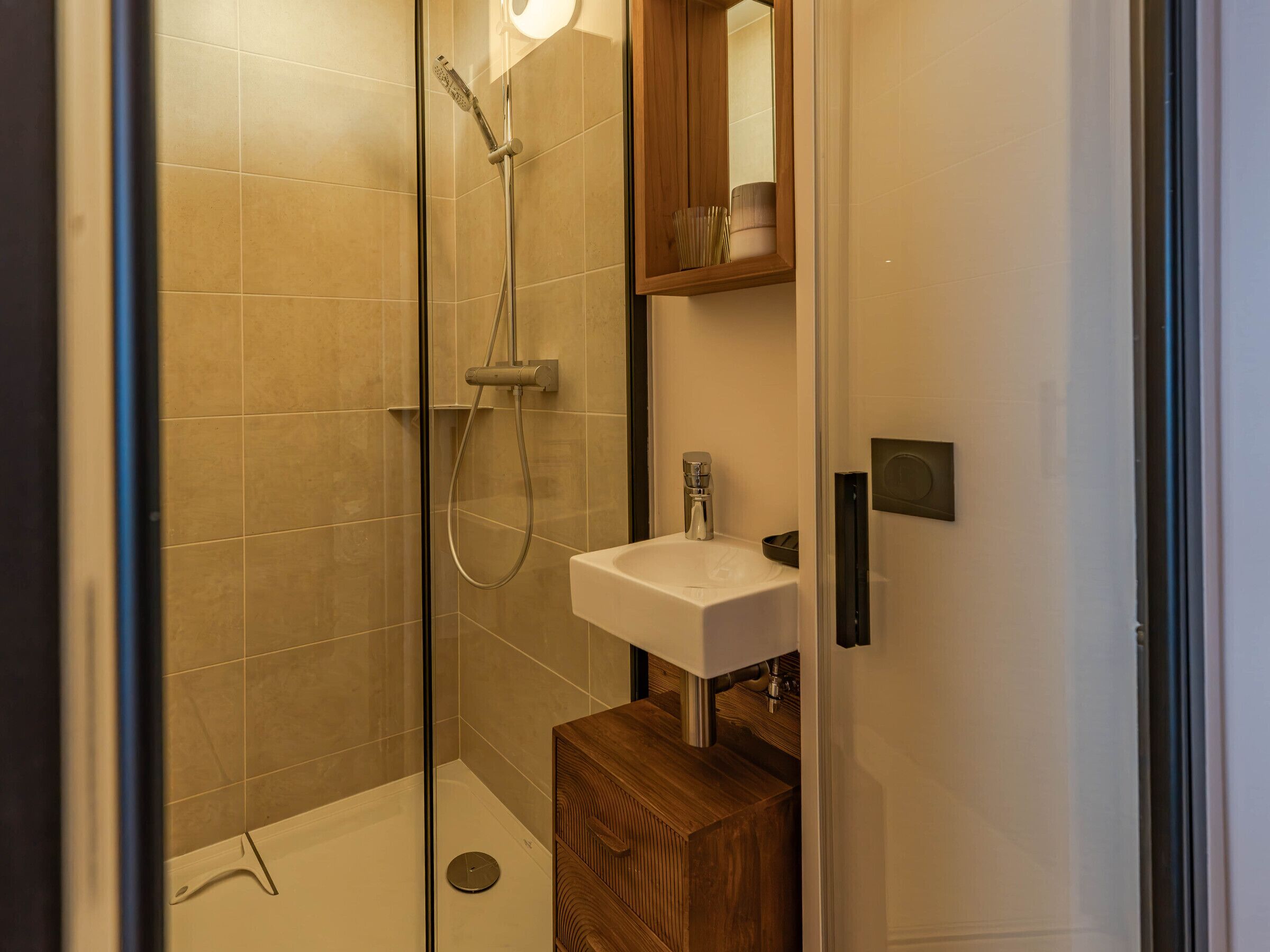 A modern bathroom with a glass shower enclosure, a wooden vanity, and a white sink.
