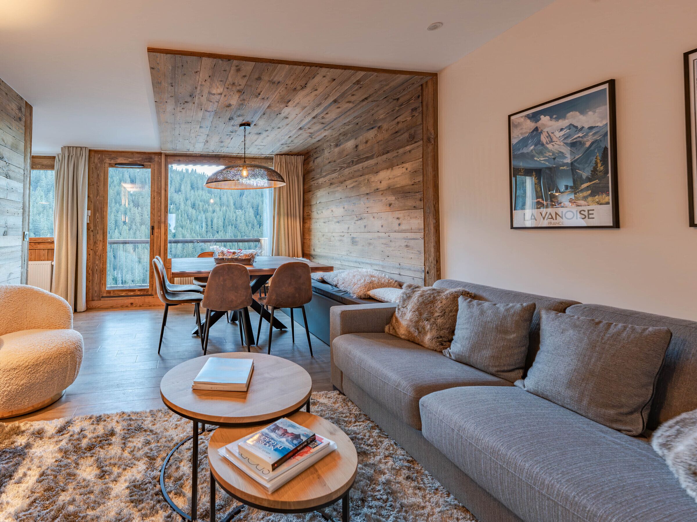 A cozy living room with a wooden ceiling, a sofa, a coffee table, and a dining area with chairs and a table.