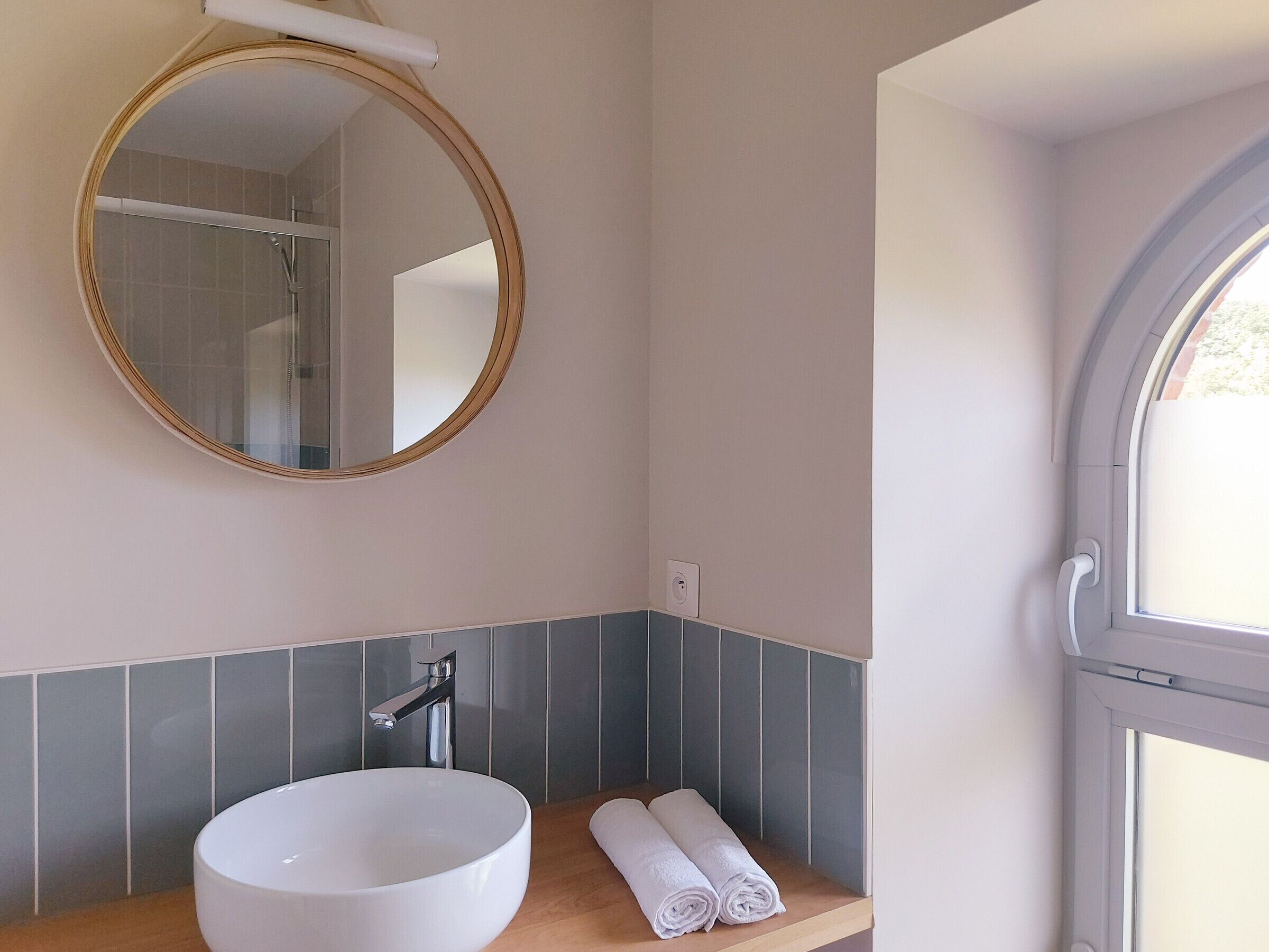 Een badkamer met een ronde spiegel, een wit wastafel en een handdoek op het aanrecht.