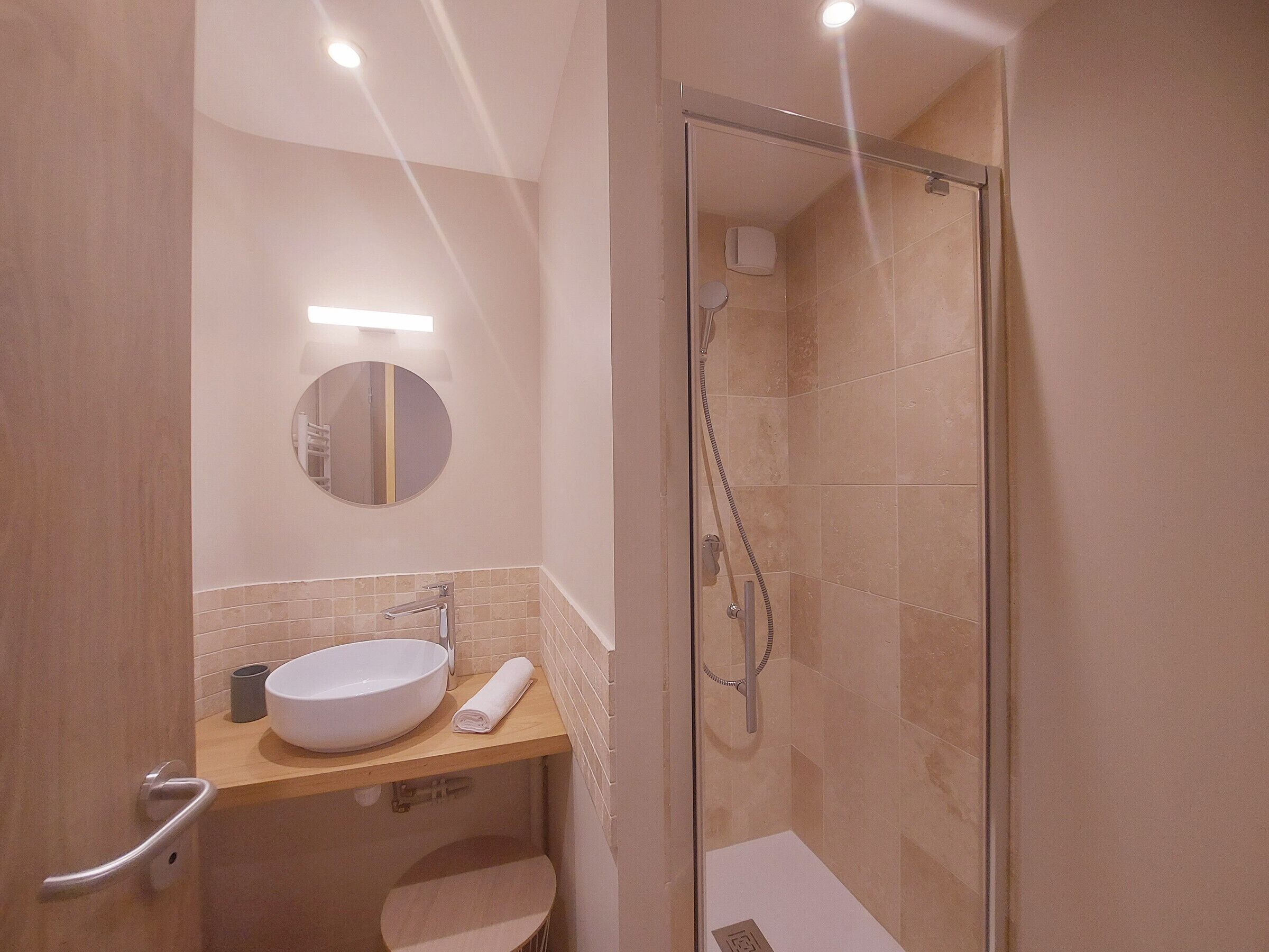 Un bany modern amb dutxa tancada per vidre, un mirall rodó i un lavabo blanc.