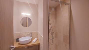 Un bany modern amb dutxa tancada per vidre, un mirall rodó i un lavabo blanc.