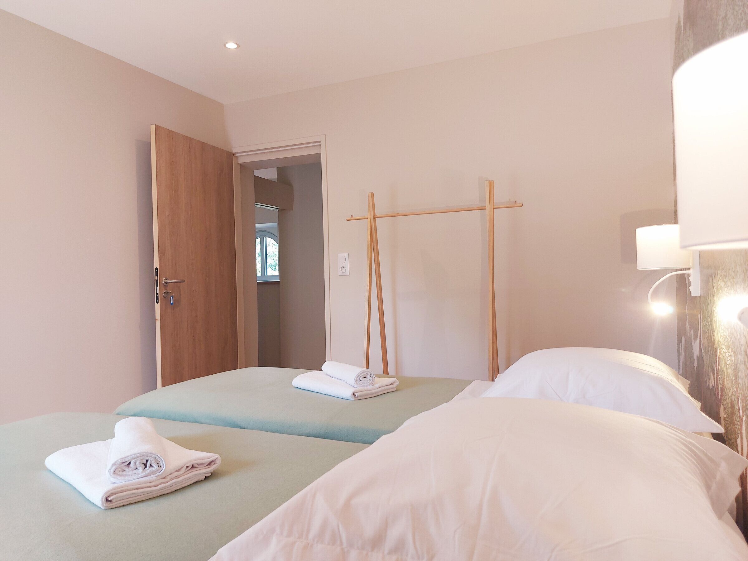 Une chambre d’hôtel avec deux lits, une porte en bois, un miroir et un luminaire fixé au mur.