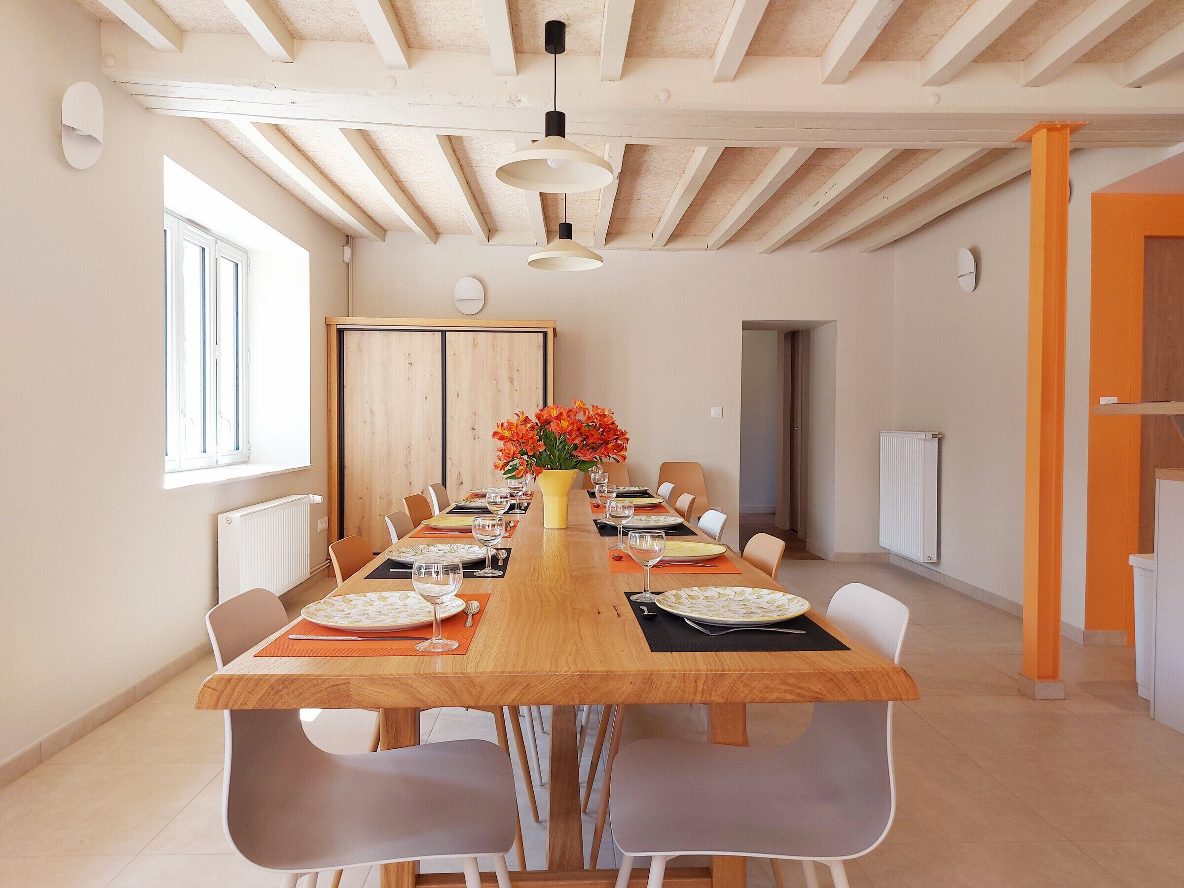A dining area with a long wooden table, white chairs, and a vase of flowers.