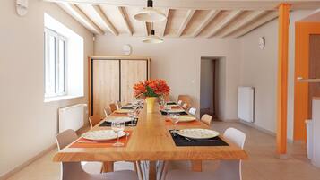 A dining area with a long wooden table, white chairs, and a vase of flowers.