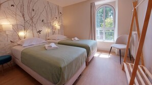 Une chambre d’hôtel avec deux lits, une fenêtre donnant sur des arbres, une chaise et une échelle en bois.