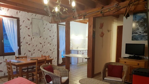 A cozy room with a bed, a dining table, wicker chairs, a television, and a painting on the wall.