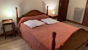 A bedroom with a wooden bed, two bedside tables with lamps, a heater, and a door.