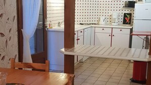A dining table with chairs, a kitchen area with cabinets and a countertop, and a tiled floor.