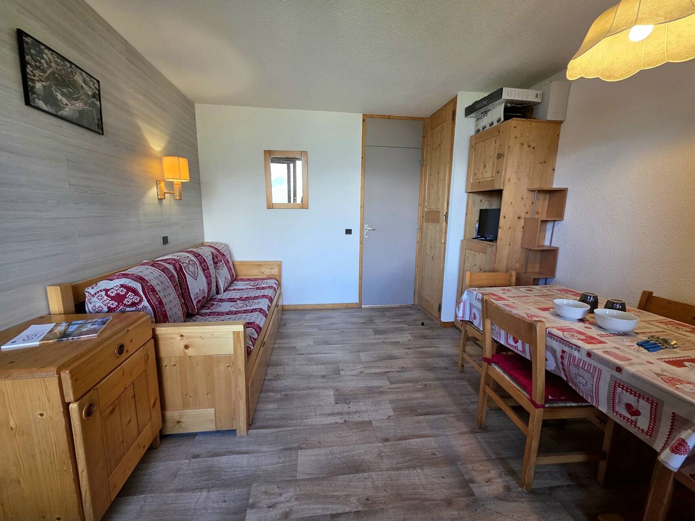 Una habitació acollidora amb un sofà de fusta, una taula de menjador amb un mantell estampat i un armari de fusta.