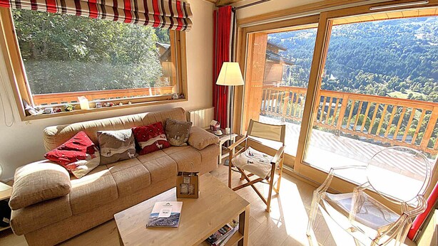 Un salon confortable avec un canapé, une table basse et un fauteuil. Il y a une fenêtre donnant sur des arbres et un balcon.