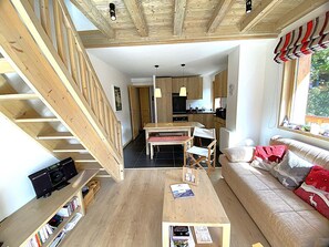 Een modern interieur met een trap, een eetgedeelte, een keuken en een woonkamer met een bank en een raam.