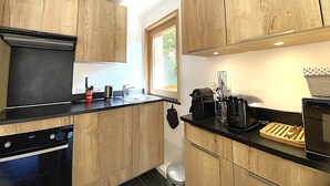 Une cuisine moderne avec des meubles en bois, un plan de travail noir, un lave-vaisselle, une cuisinière et une fenêtre qui laisse entrer la lumière naturelle.
