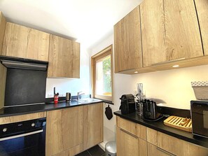 Een moderne keuken met houten kastjes, een zwart aanrecht, een vaatwasser, een fornuis en een raam dat voor natuurlijk licht zorgt.