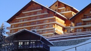Un bâtiment en bois à plusieurs étages, doté de balcons, qui ressemble probablement à un hôtel ou à un complexe touristique, avec un ciel bleu clair en arrière-plan.