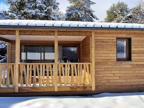 A wooden cabin with a balcony, large windows, and a door.