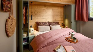 A bedroom with a wooden ceiling, a bed with pink bedding, a nightstand with a coffee maker, and a hanging bag. - Cozy chalet for 6 in nature (Aussois)