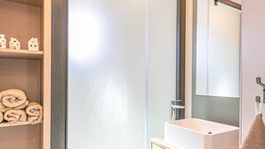 A modern bathroom with a white sink, a mirror, and a shelf with rolled towels. - Cozy chalet for 6 in nature (Aussois)