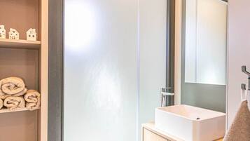 Une salle de bain moderne avec un lavabo blanc, un miroir et une étagère où sont pliés des serviettes.