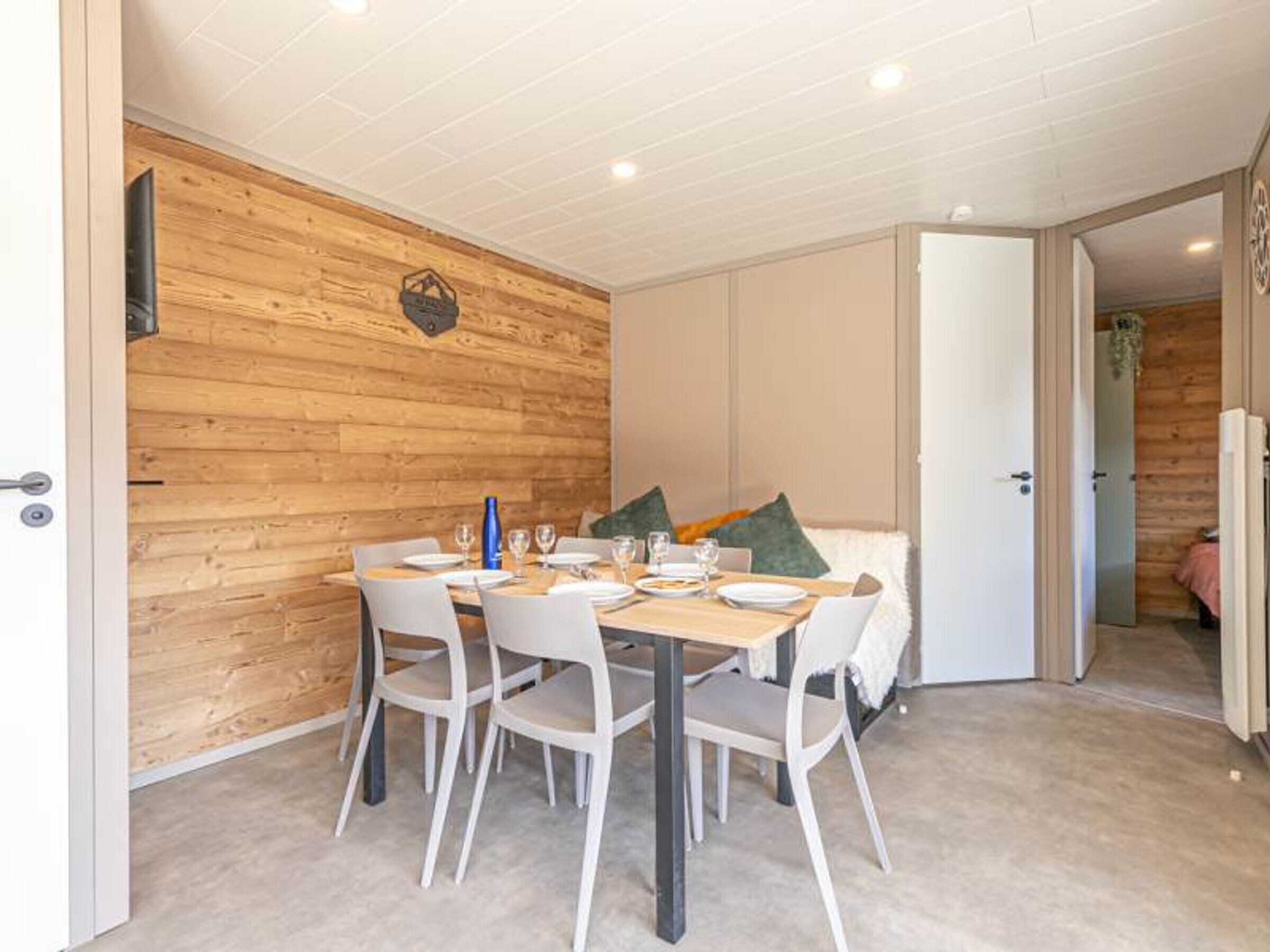 Un coin repas avec un mur en bois, une table dressée pour quatre personnes et un canapé en arrière-plan.