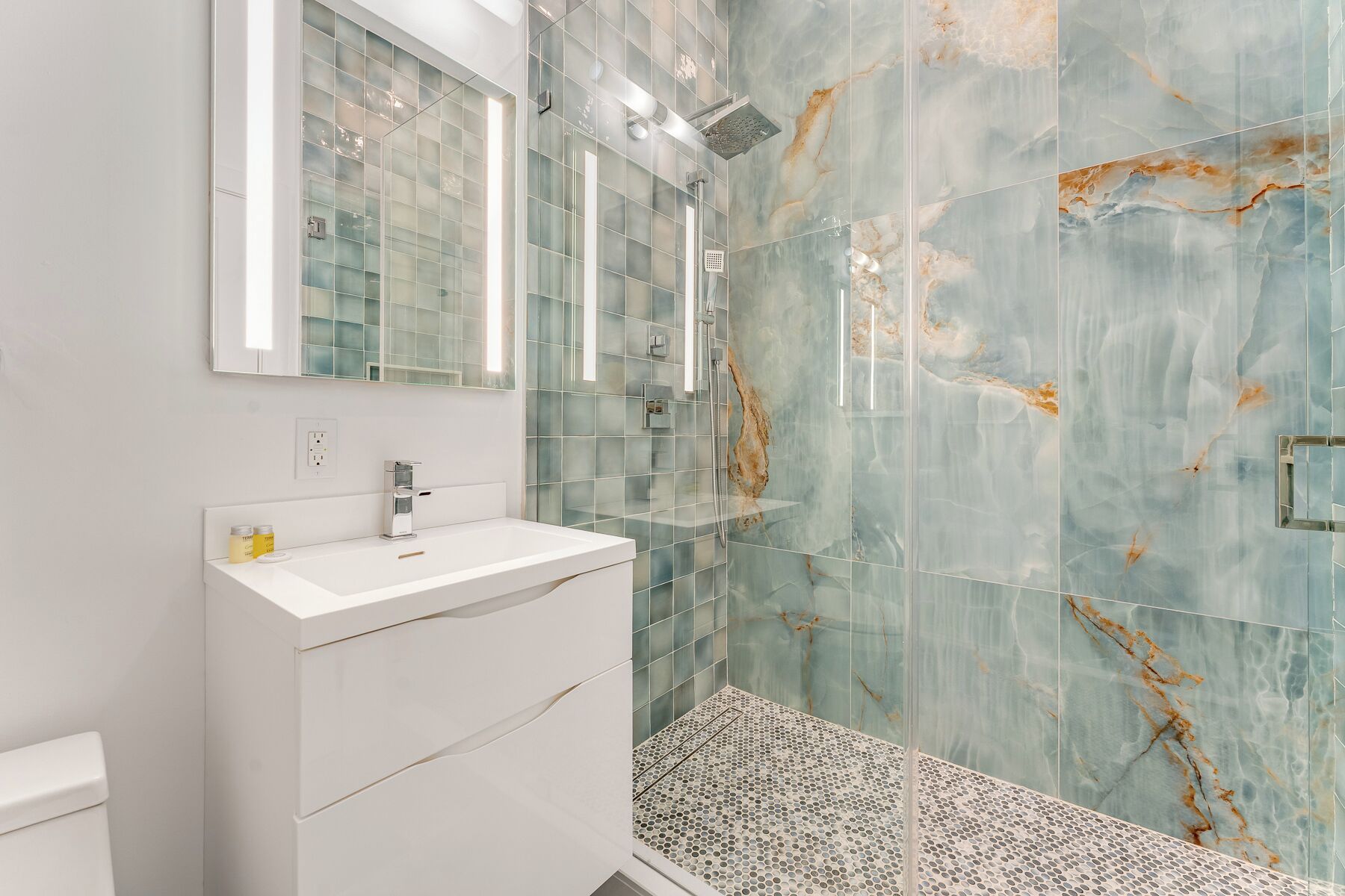 A bathroom with a white vanity, a glass shower enclosure, and a marble-patterned wall.