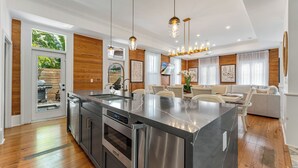 A modern kitchen with a central island, stainless steel appliances, and a dining area with a sofa and chairs. - THE BLUE PINEAPPLE ~ Old Town 4 BR/4.4 Bath Home w/ Private Pool & Parking! (Key West)