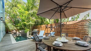 A wooden deck with a pool, outdoor furniture, and a wooden fence with hanging decorations. - THE BLUE PINEAPPLE ~ Old Town 4 BR/4.4 Bath Home w/ Private Pool & Parking! (Key West)
