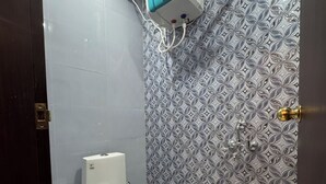 A bathroom with a toilet, a wall-mounted air freshener, and patterned tiles. - Hotel Anmol Inn (Karchana)