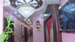 A hallway with a chandelier, a potted plant, a small shrine, and a television screen. - Hotel Anmol Inn (Karchana)