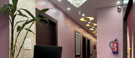 A reception area with a modern design, featuring a reception desk, a large chandelier, and a fire extinguisher mounted on the wall.