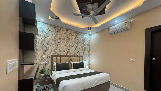 A modern hotel room with a bed, bedside table, and a ceiling fan. - Hotel Anmol Inn (Karchana)