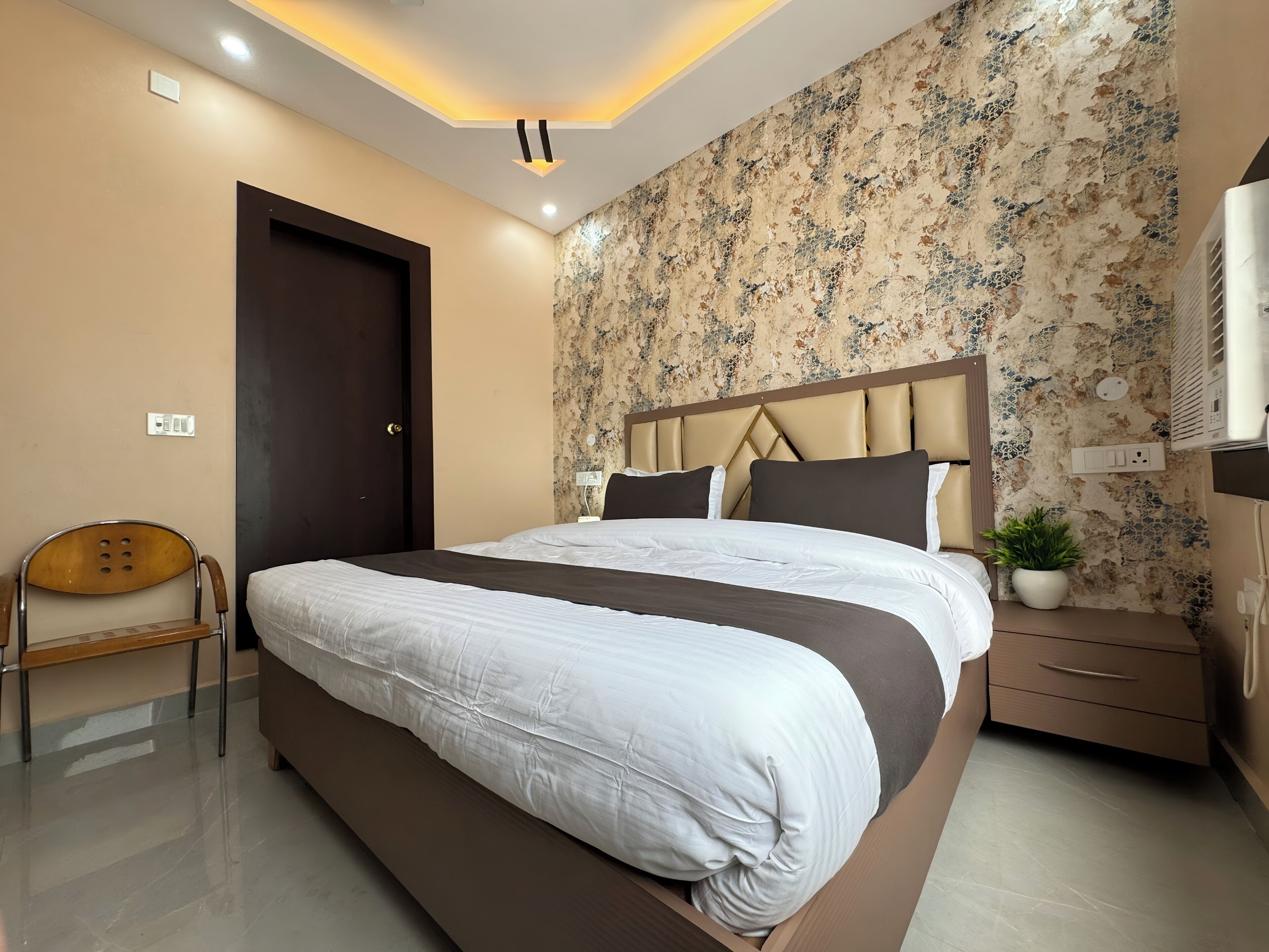 Un dormitorio moderno con una cama grande, una silla de madera, una mesita de noche y una planta en maceta.